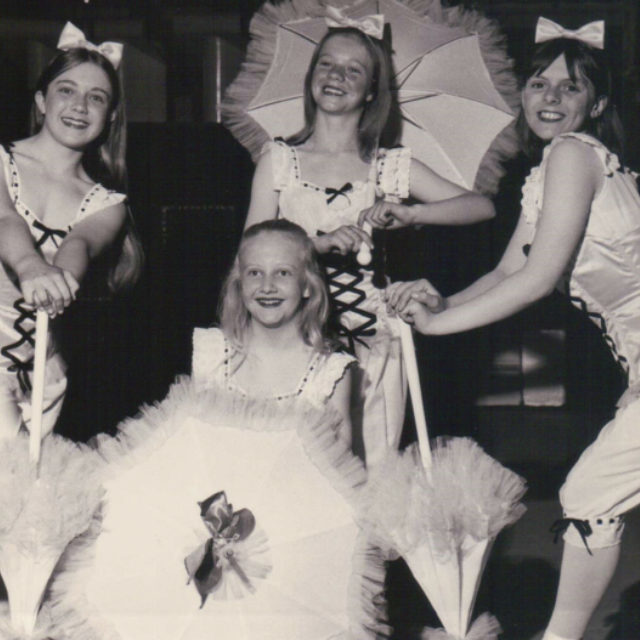 A group of four girls posed in a group holding parasols.