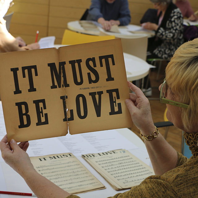 Volunteer holding sheet music with the words "It must be love"